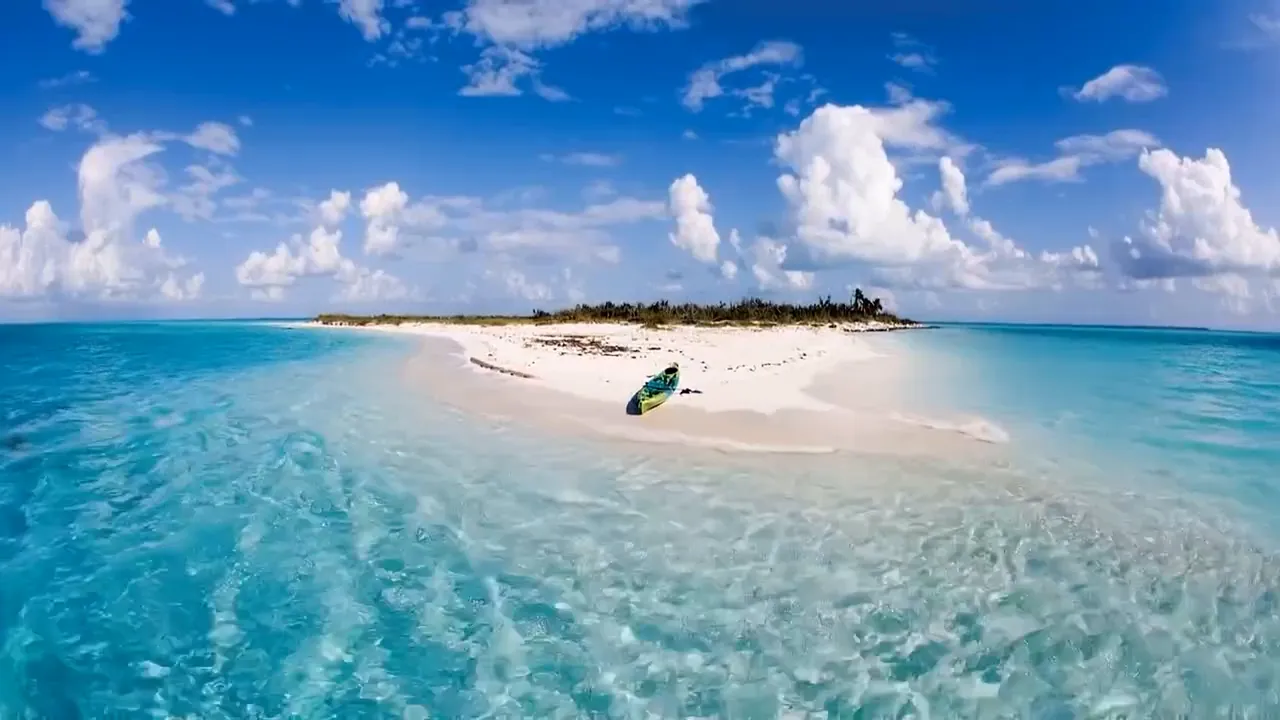 White sand cay with a kayak on the beach, surrounded by clear turquoise shallows in the Bahamas